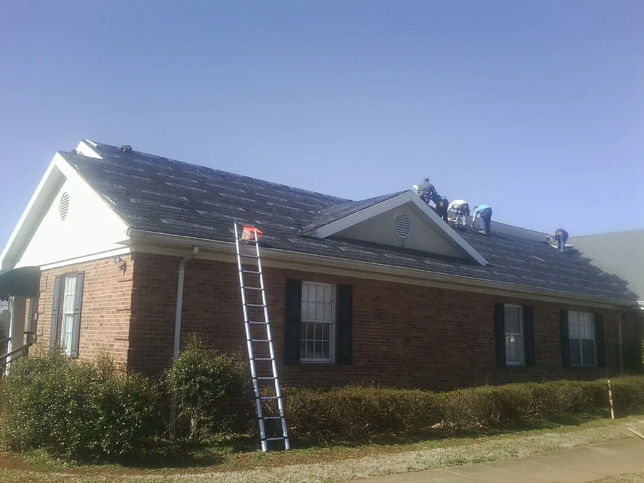 Crew tearing shingles off a brick ranch roof with a ladder set — Emergency Roof Repair work by our crew in Stephens City