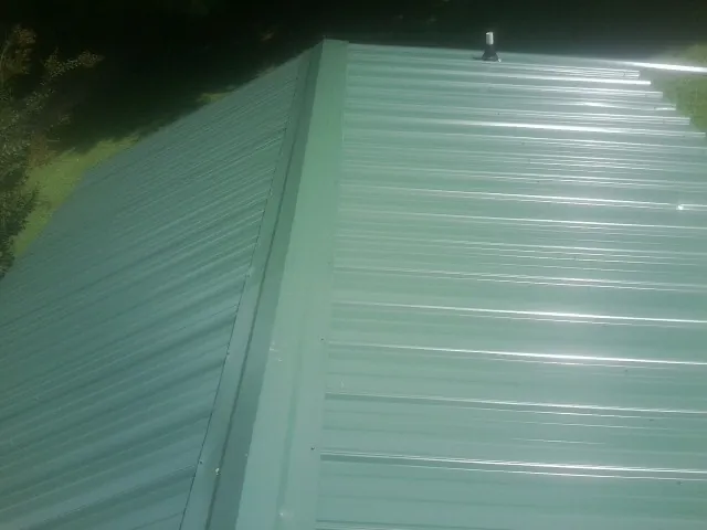 New green metal panels meeting at the ridge of a roof — Flat Roof Repair work by our crew in Stephens City