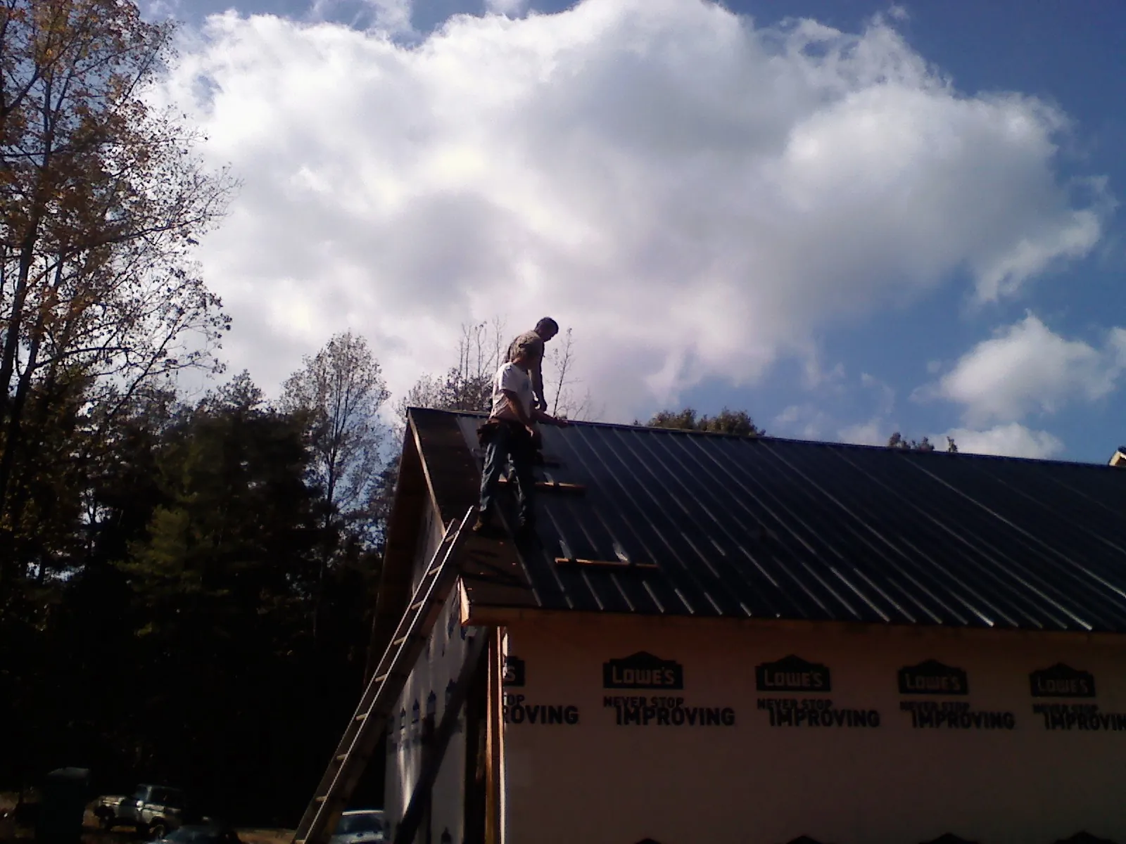 Roofer fastening dark metal panels high against a cloudy sky, from a Roof Inspection job in Stephens City