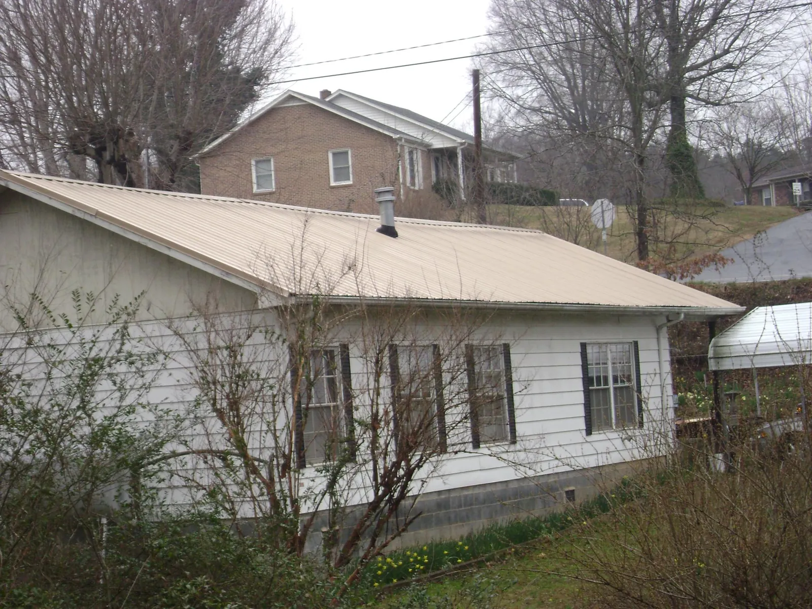 Tan metal roof on a white sided house set into a hillside — Commercial Roofing by Roofing Brothers in Stephens City